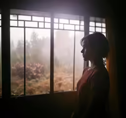 a woman standing by a window looking out