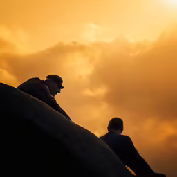 two men sitting on top of a rock next to each other