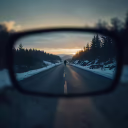 the rearview mirror of a car as it travels down a road with trees