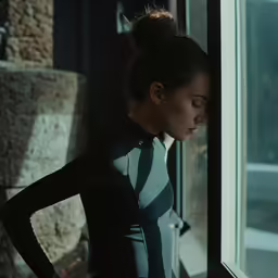 a woman with her hand on the hips looks out a window