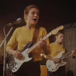 two people playing guitars in front of a microphone
