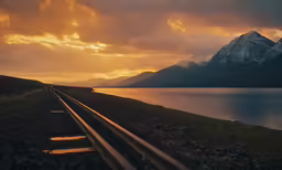 the train tracks pass the mountains as the sun sets