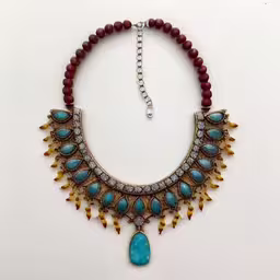 a necklace that has a large pendant attached,necklace on white background with red beads and turquoise stone,a very pretty blue and gold statement necklace,a blue stone hangs from a gold plated necklace,an image of a beautiful necklace