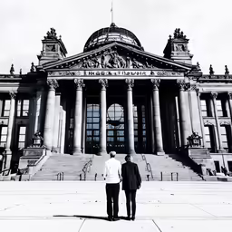 two men in business suits stand in front of a building