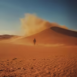 person hiking through sand dunes with dust blowing from the top