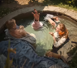 some people sitting in a body of water with one holding their hands up