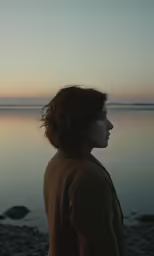 a woman stands next to the water at sunset