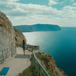 a woman walking up a narrow path toward the ocean