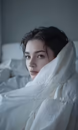 a woman wrapped up in blankets sitting on a bed