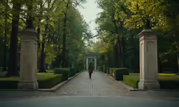 man walking down an empty pathway between two concrete pillars
