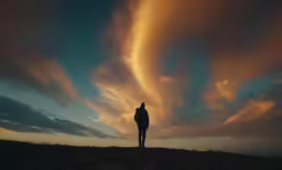 a person in the evening standing on a hill under a cloudy sky