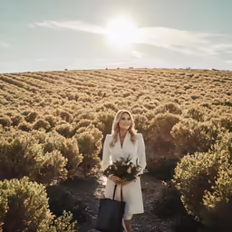 a woman is walking through a field holding a bouquet