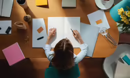 a woman writing on top of some white sheets