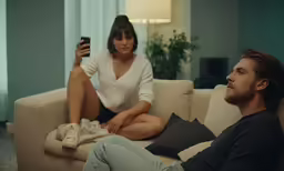 the young man and woman are sitting on the couch with a blanket
