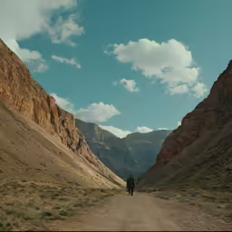 person in distance standing on road in mountains near rocky landscape