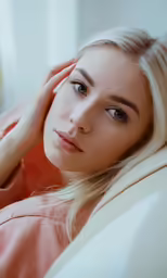 young blonde woman in orange top with hand on her ear