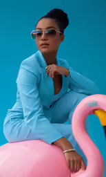 an image of a woman wearing sunglasses sitting on a fake flamingo