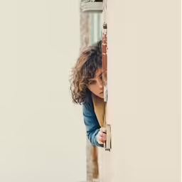 a girl peeking out from behind a wall with her head in the doorway
