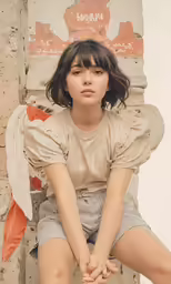 a woman wearing short grey shorts, sits on a pillar and poses for a photo