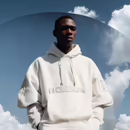 a man wearing a white hoodie standing in front of clouds