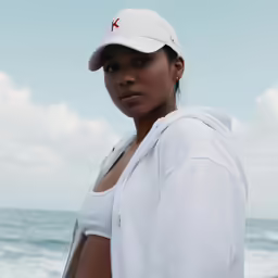 a woman with a red cross on her cap poses for a photo at the beach