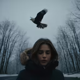 a woman is standing in the snow watching an eagle fly by