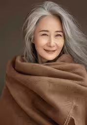 the woman is smiling and wearing a tan blanket,an elderly woman wrapped up in a blanket