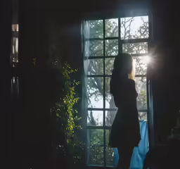 the woman is standing by a window in the dark
