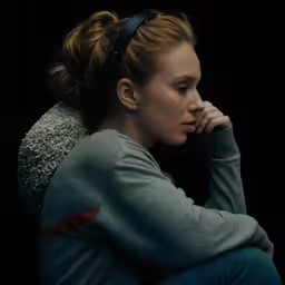 the young woman is sitting on the floor with her hand on her cheek