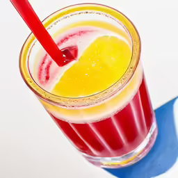 a red glass has a beverage, some lemon wedges and a straw