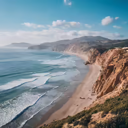 a beach with sand and a cliff next to the ocean