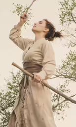 a woman in historical dress holding a wooden stick
