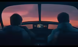 two men sit in the cockpit of a helicopter and watch a sunset