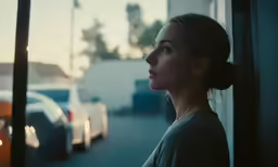 a woman standing near some windows looking out the window