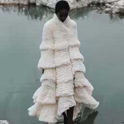 a black woman in an animal coat standing near a lake