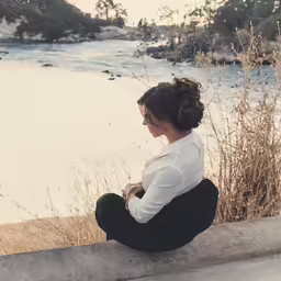 the woman is sitting on the ledge looking at the water
