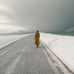 a woman wearing a yellow coat walking on the side of a road with a dark cloudy sky