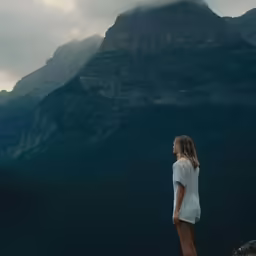 a woman is looking out at a mountain while standing on a rocky hill