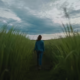 a woman walking through a field of tall grass