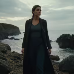 the blackcoat and grey top worn by a woman walks along the sea coast