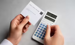 a person is holding a calculator and taking notes