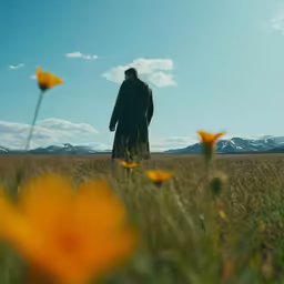 a man standing in a field of tall grass with flowers in the foreground
