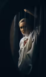 a woman wearing white poses behind bars in the dark