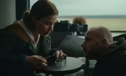 two people sit at a table, one eating food