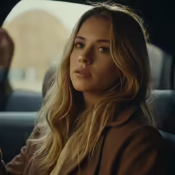 a woman sitting in the back seat of a car holding a cigarette
