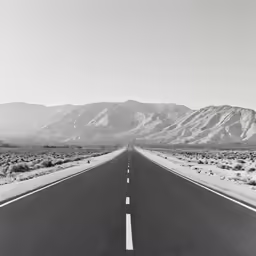 black and white photo of an empty highway with mountains in the background