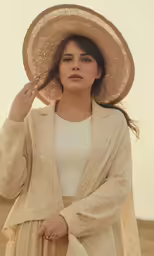 a woman in a beige suit and hat holding her hat