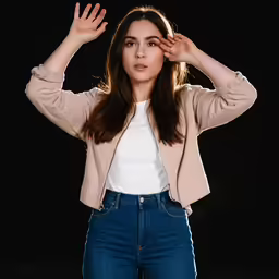 a girl posing in front of a black background, holding her hands on top of her head