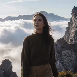 a woman standing on the side of a mountain in front of a cloudy valley