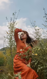 a woman in an orange dress poses in a field